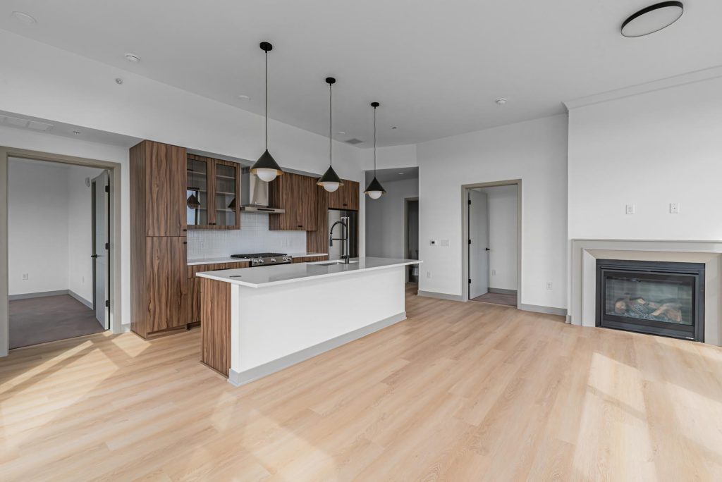 Open kitchen with wood cabinets, island, pendant lights, and nearby fireplace