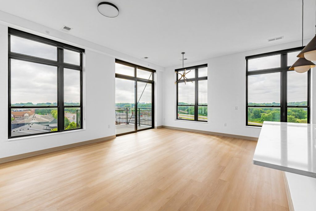 Spacious living room with wood floors, floor-to-ceiling windows, and balcony access