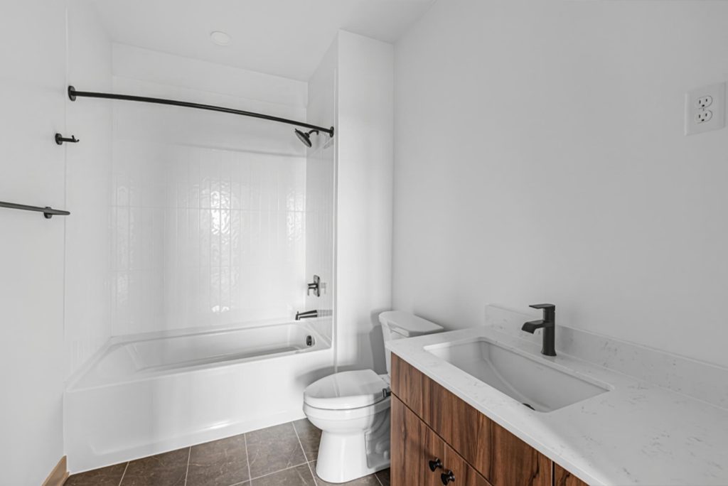 Apartment bathroom with tub shower, white tile surround, modern vanity, and matte black fixtures